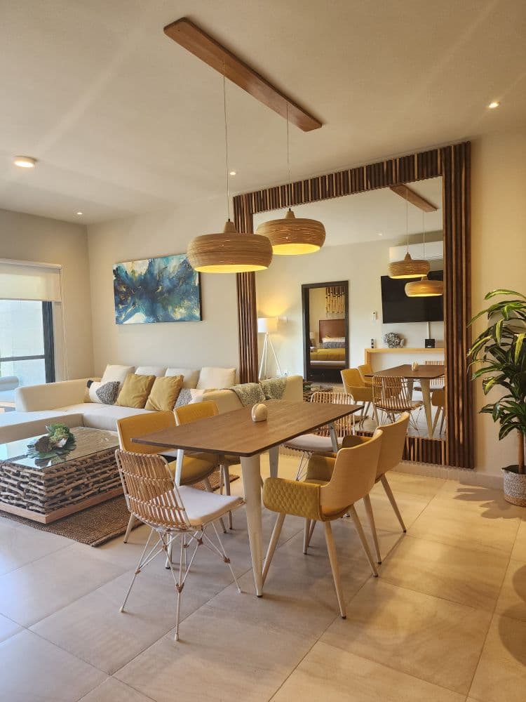 A furnished living and dining room with a cream sofa, a wooden table and woven pendant lights.